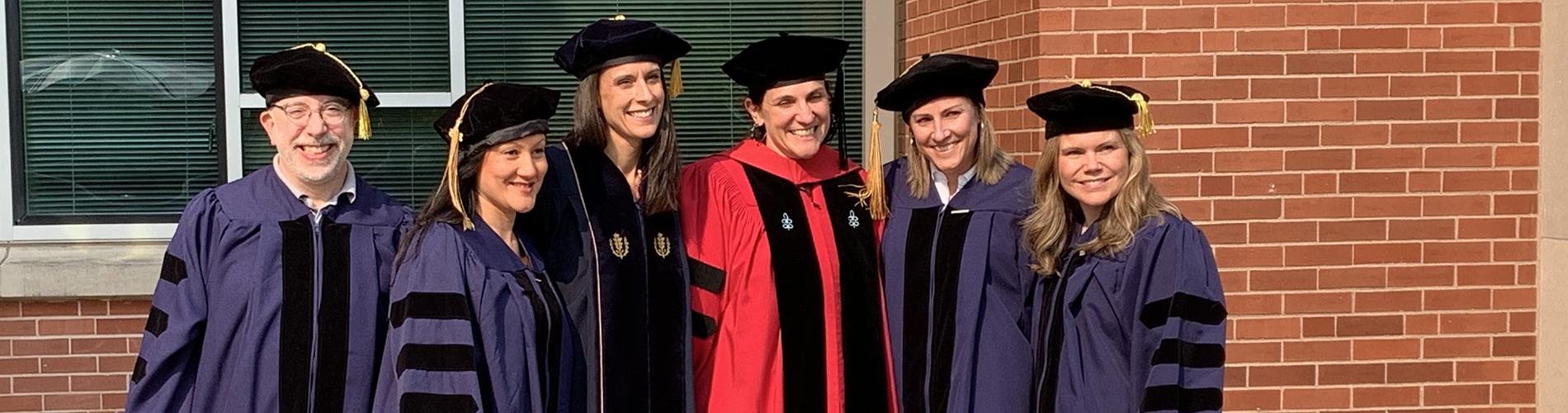 Class of 2023 Ed.D. graduates stand in a row with a faculty member while wearing their doctorate robes.