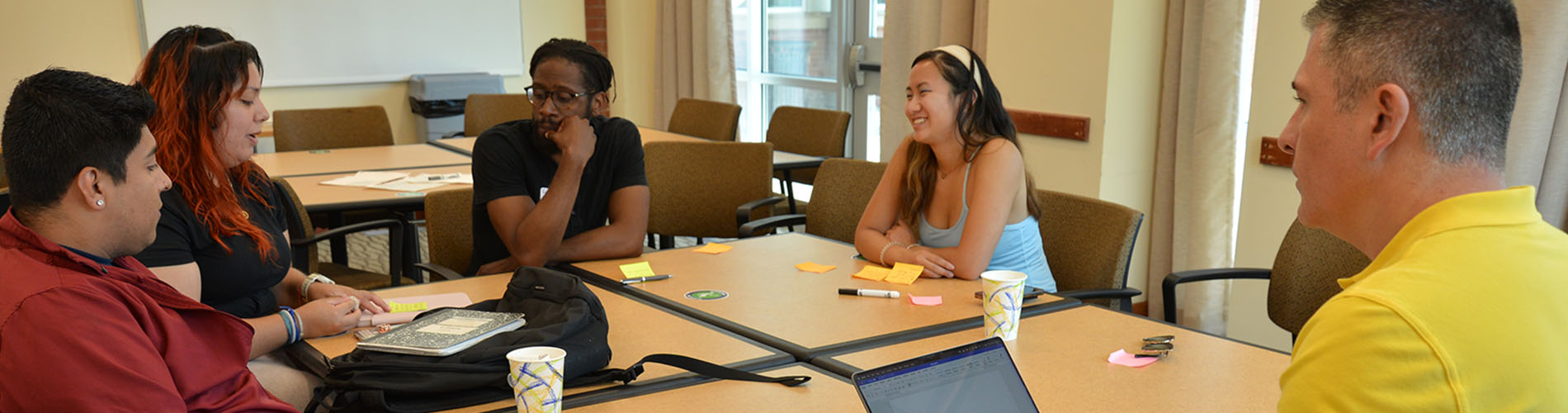 Four adult students and a professor sit at a table and talk.