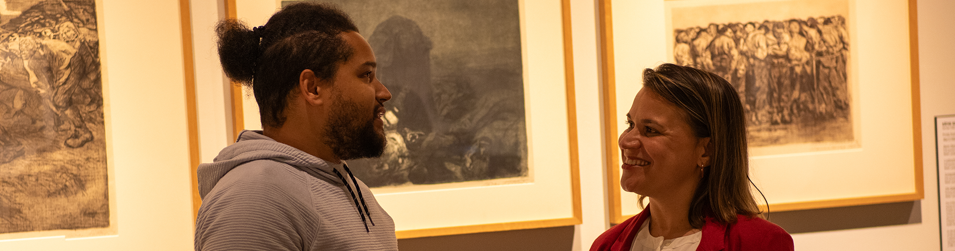 Two adults stand in an art gallery and converse