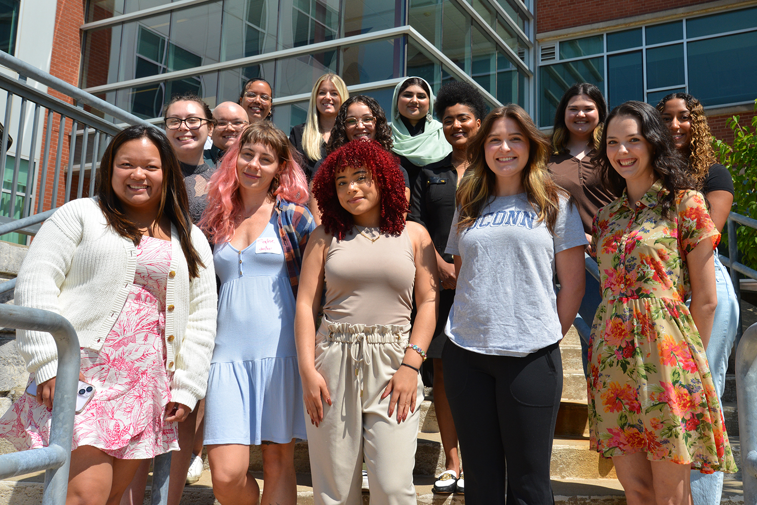 Fourteen graduate students stand in a group on the steps outside the Gentry Building.